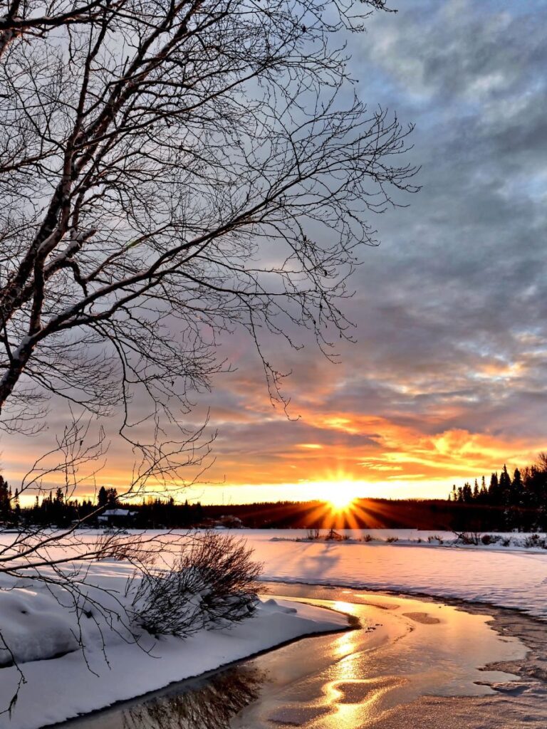 sun rising over a landscape covered in snow with an icy stream flowing by