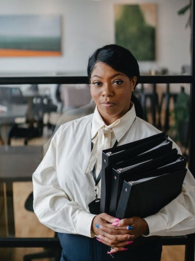 professional looking woman holding a large stack of black binders in an accounting office