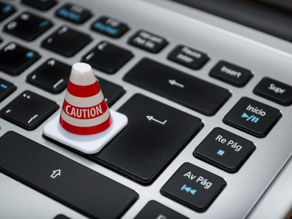 A mini traffic cone with red and white stripes says “Caution” as it sits on top of a laptop keyboard.