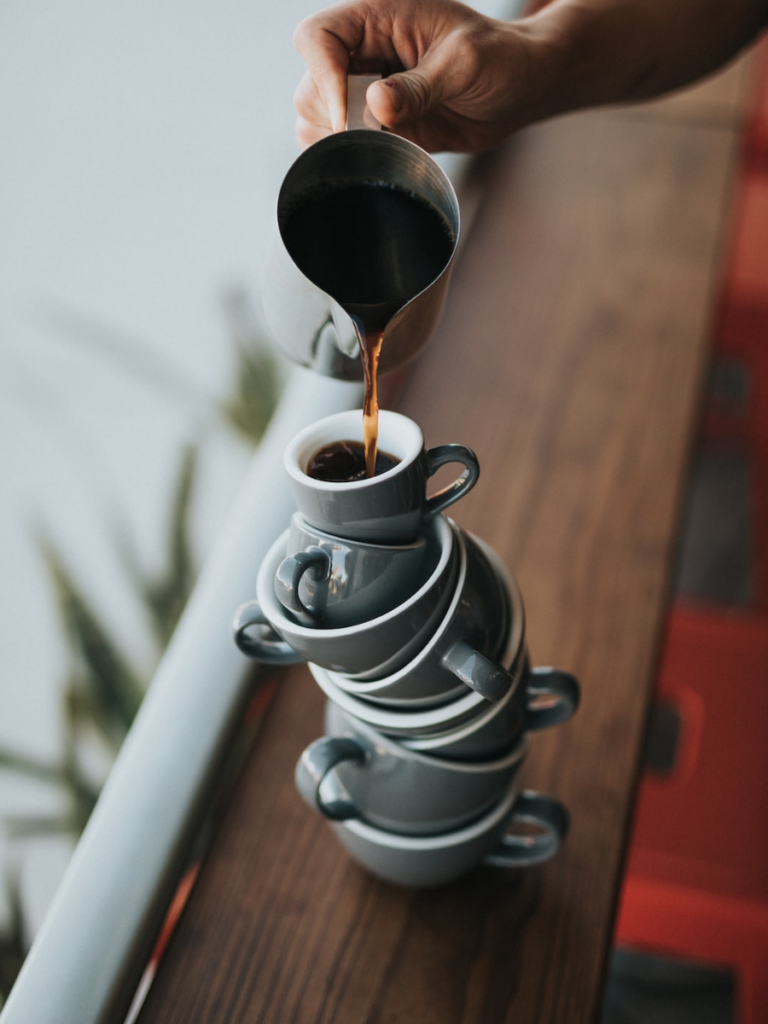 a pile of teacups and saucers precariously balances as someone pours coffee into the top one