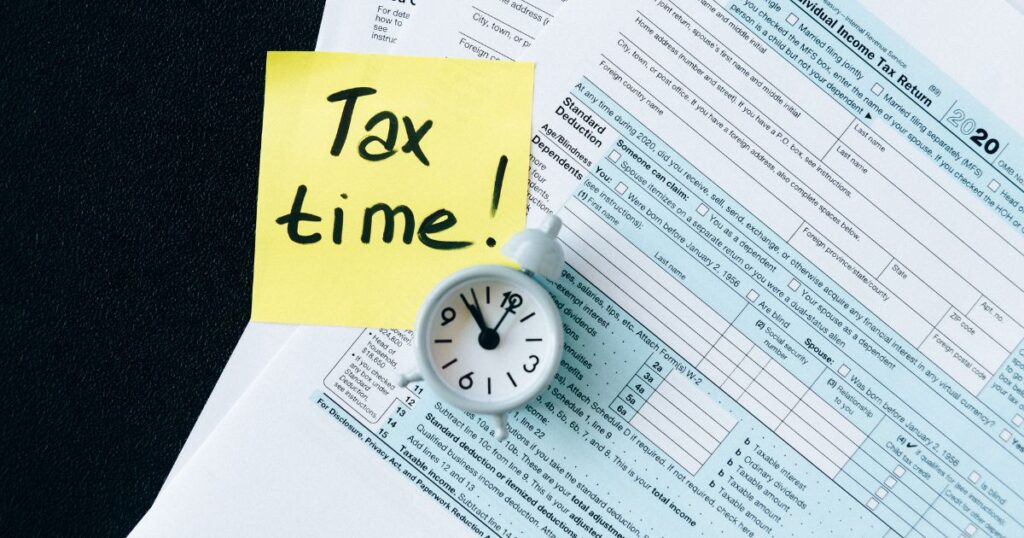 USA tax forms with a yellow sticky note that says, “Tax Time!” and a blue clock