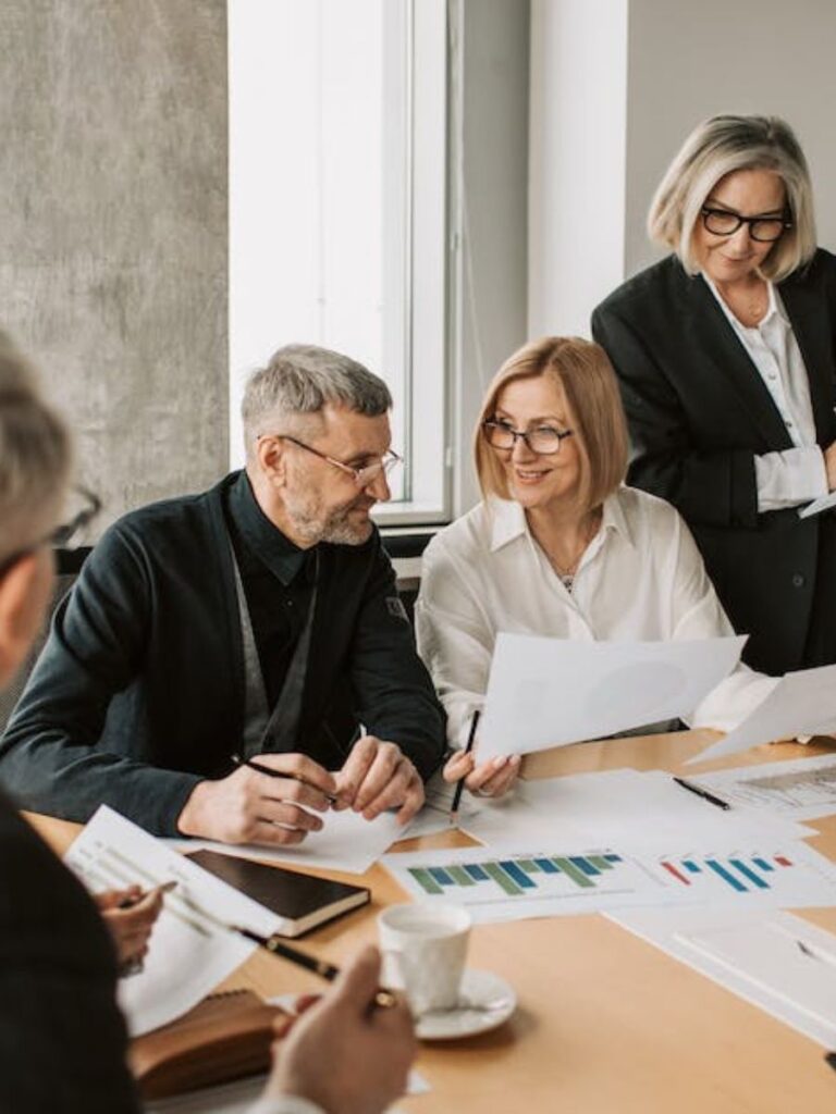 group of people in a meeting discussing finances surrounded by graphs of projections and reports