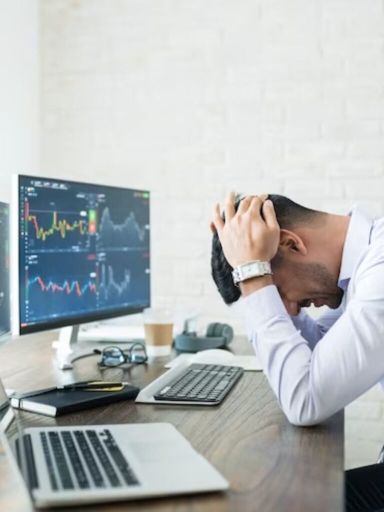 a man sits dejected in front of a trading computer screen with his head in his hands