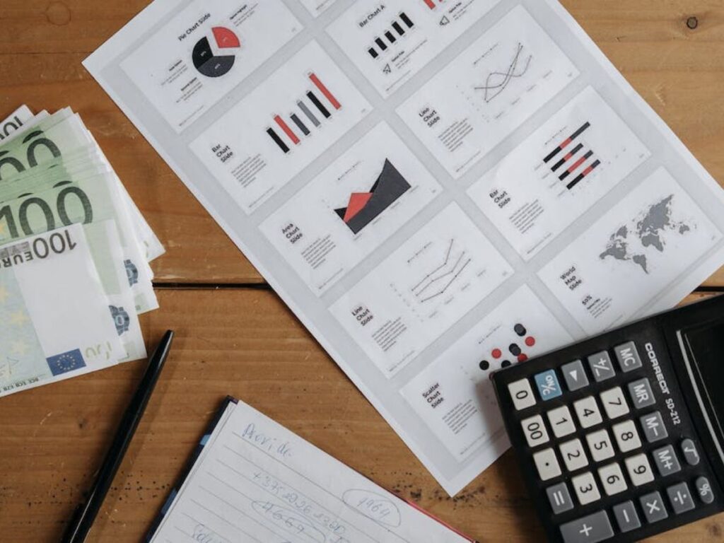 items for getting taxes organized on a table including a calculator, a pile of local currency, a notebook, and a financial report