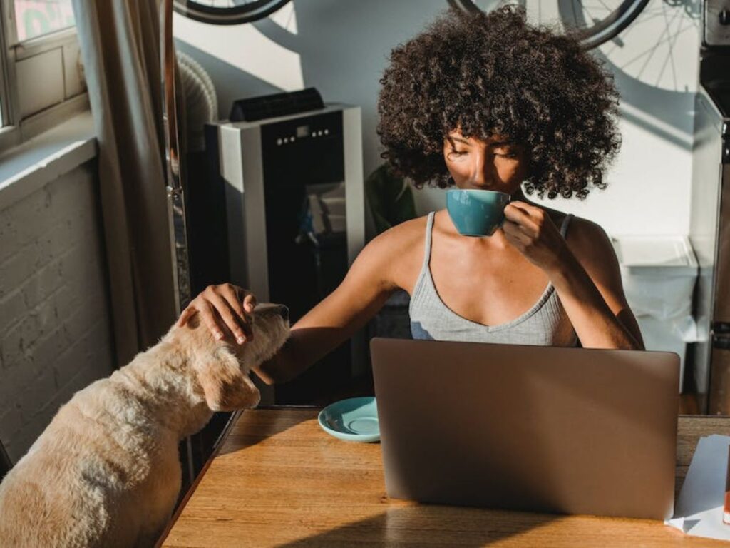 woman confidently sipping her coffee as she pets her dog and looks at her computer