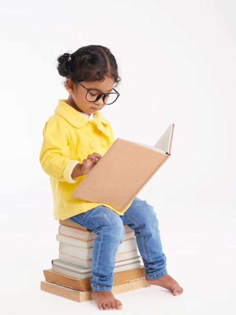 cute young girl with big glasses reads a book while sitting on top of a stack of books