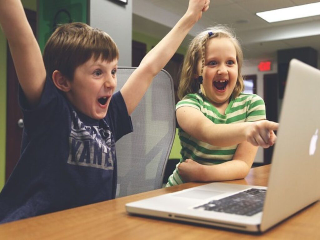 two kids celebrate something exciting on a computer with lots of expression